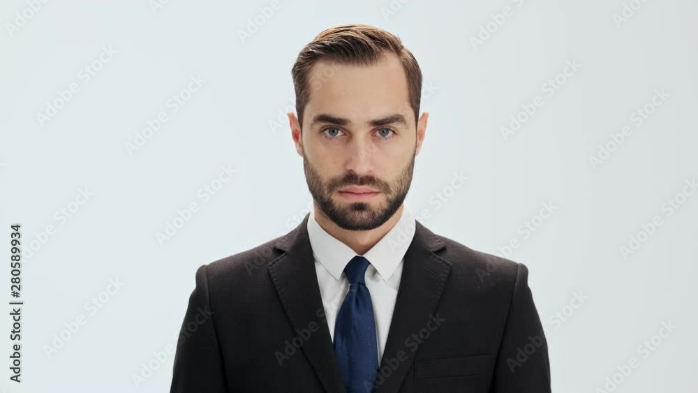 Serious young businessman in black suit and blue tie raising his head and looking at the camera over gray background isolated Serious young businessman in black suit and blue tie raising his head and looking at the camera over gray background isolated