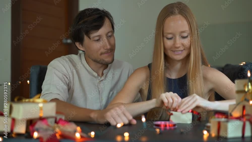 Slowmotion shot of a young woman and man father and mother wrap presents. Presents wrapped in craft paper with a red and gold ribbon for Christmas or new year. Parents make an advent calendar for Slowmotion shot of a young woman and man father and mother wrap presents. Presents wrapped in craft paper with a red and gold ribbon for Christmas or new year. Parents make an advent calendar for