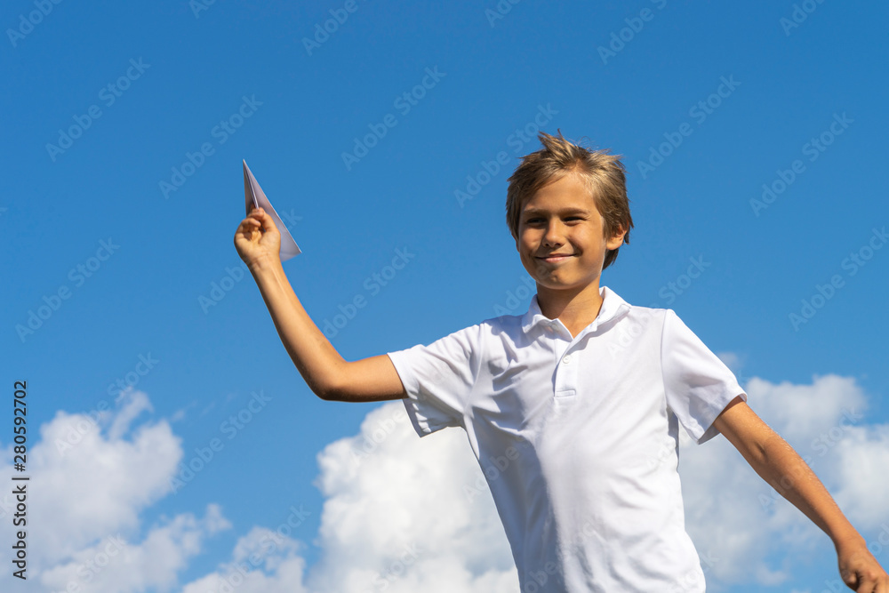Happy kid playing with paper airplane against blue summer sky background Happy kid playing with paper airplane against blue summer sky background