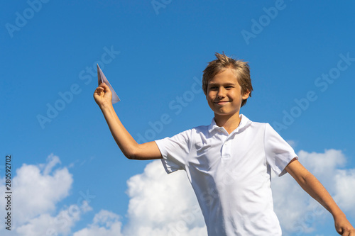 Happy kid playing with paper airplane against blue summer sky background