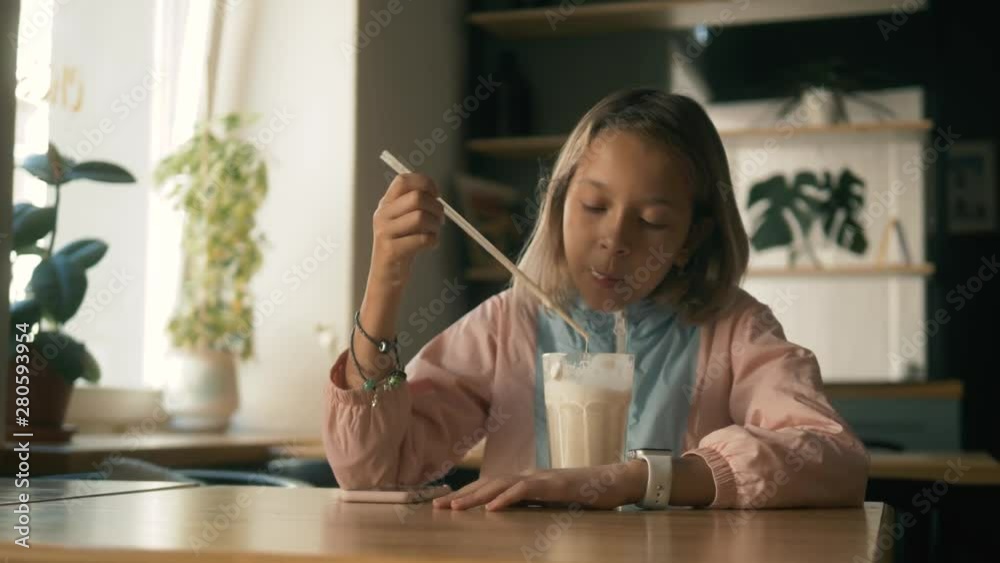 Beautiful girl in sitting in cafe counter and drinking milkshake while taking cute photos on her cellphone, child kid after lessons with cellphone Beautiful girl in sitting in cafe counter and drinking milkshake while taking cute photos on her cellphone, child kid after lessons with cellphone