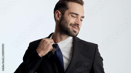 Exhausted young businessman in black suit and blue tie feeling tired and loosening his tie while looking at the camera over gray background isolated