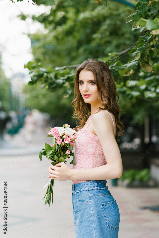 Romantic image of a young girl walking on a summer street in the Park with a bouquet of roses, city recreation and walk. Portrait