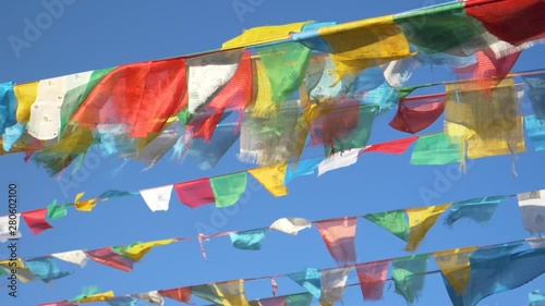 SLOW MOTION, CLOSE UP: Prayer flags hanging off ropes spanning across Himalaya flap in the strong winds. Cinematic shot of vibrant buddhist flags waving above the Tibetan landscape on a sunny day.