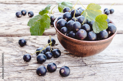Fresh ripe currant berries in a bowl on wooden background near green leaves. Juicy fruits currants. Black currant