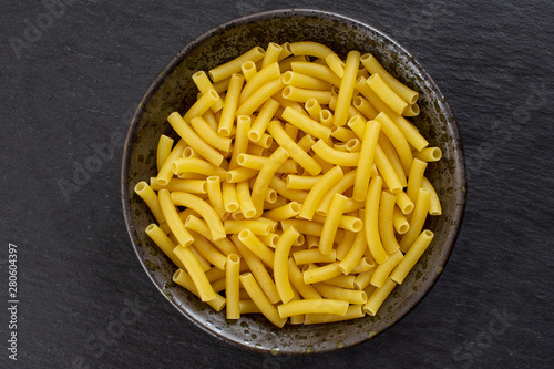 Lot of whole raw pasta macaroni on grey ceramic plate flatlay on grey stone