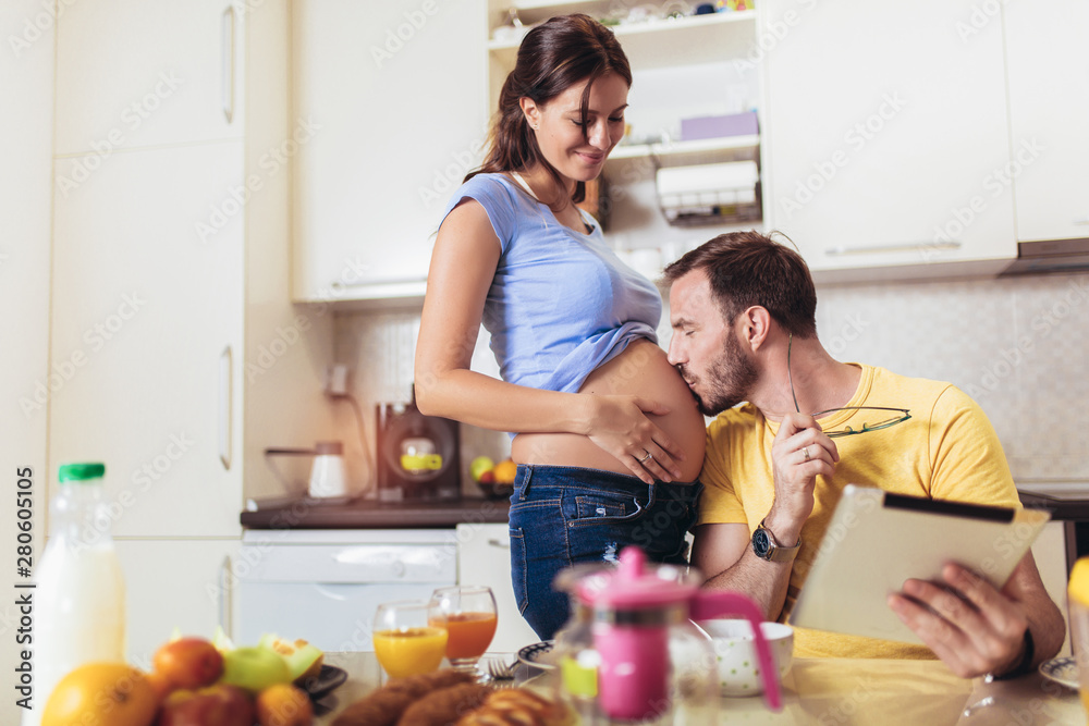 Pregnant woman with husband in the kitchen using digital tablet. Pregnant woman with husband in the kitchen using digital tablet.