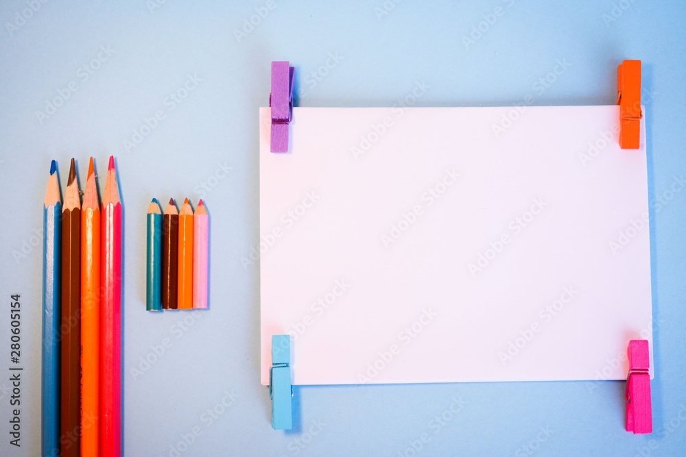 Large and small colored pencils on the table next to a white postcard for writing Large and small colored pencils on the table next to a white postcard for writing