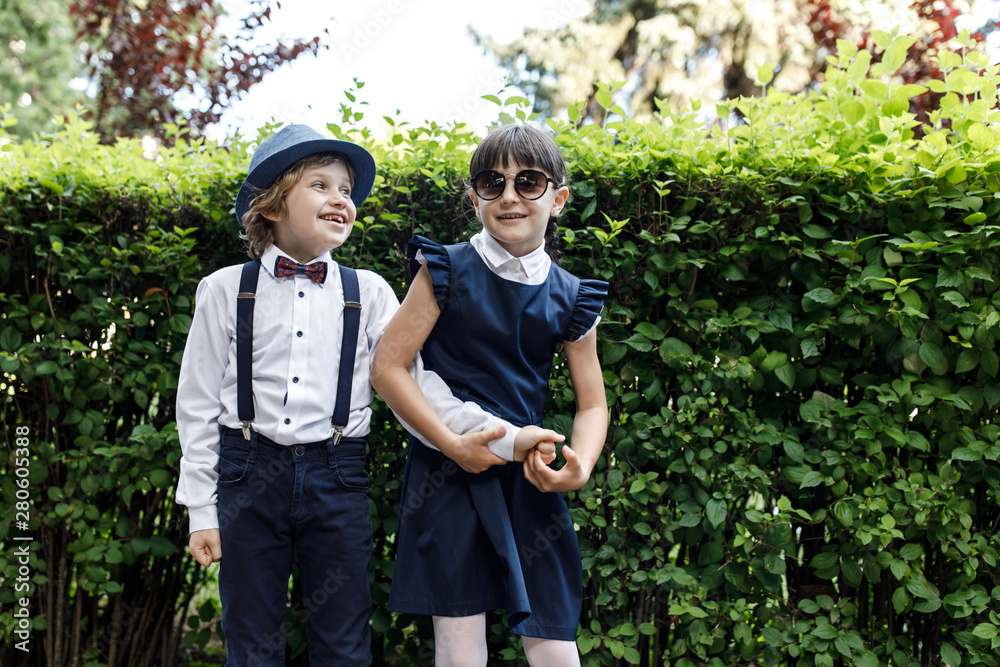 Cute blond guy and cute girl, school year fun time outdoors. Children dressed in school uniform play games in the park Cute blond guy and cute girl, school year fun time outdoors. Children dressed in school uniform play games in the park