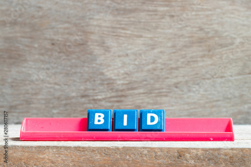 Tile letter on red rack in word bid on wood background photo