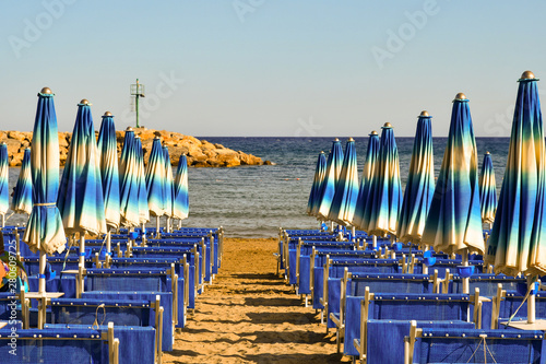 View of a sandy beach with rows of deck chairs and sun umbrellas with the sea in the background in summer, Diano Marina, Imperia, Liguria, Italy photo