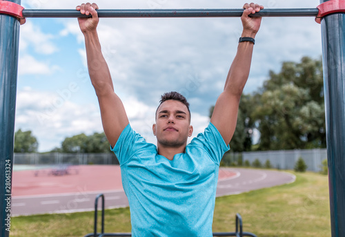 Athletic man in summer in city, pulls up on bar, a healthy lifestyle fitness workout, workout in fresh air. The concept of strength and motivation for success. Lifestyle of young generation.