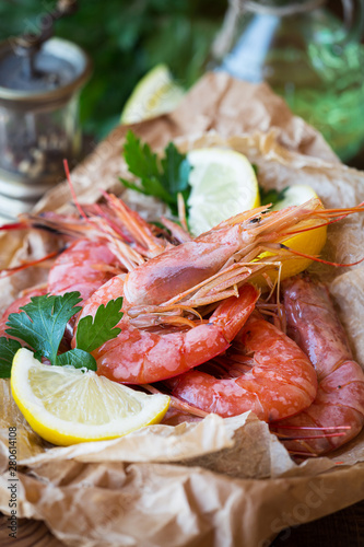 Steamed tiger prawns or shrimps on a fishmoger parchment paper with lemon wedges and fresh parsley leaves