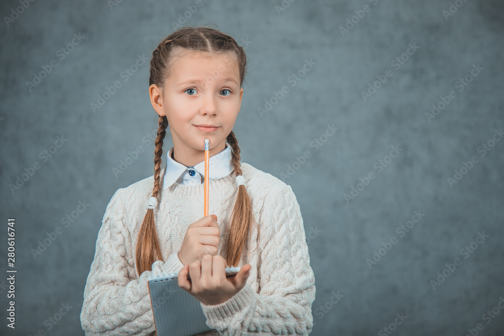 A confused girl is thinking about her homework is isolated on grey backgrounds. A confused girl is thinking about her homework is isolated on grey backgrounds.