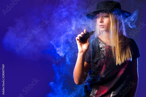 Vape. The girl in the black hat inhaling from vape. Vapor. Smoking vape. Vaping concept. E-Cigarette. Electronic Cigarette.