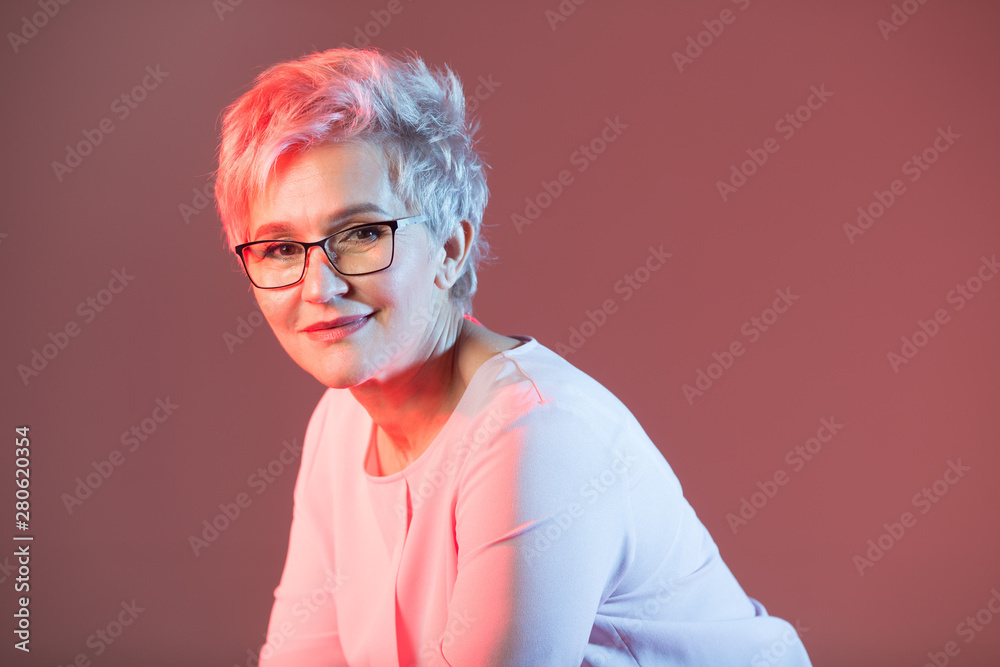 beautiful stylish woman in age, with glasses with a short haircut on a pink background