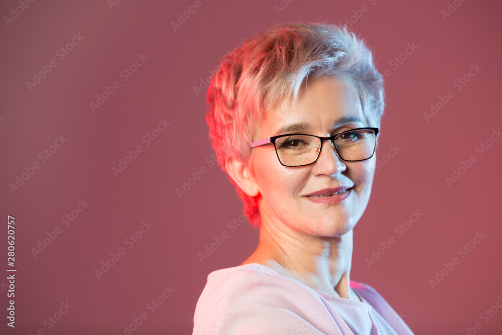 beautiful stylish woman in age, with glasses with a short haircut on a pink background