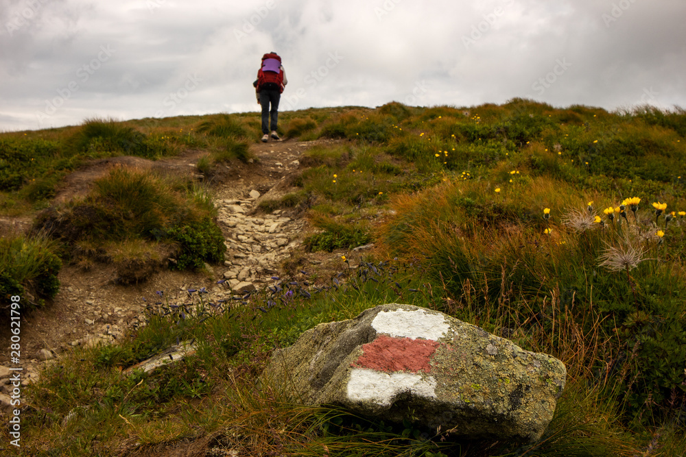 Obraz premium Young girl with backpack trekking in mountain route. Route mark in foreground.