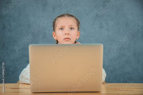 Cute elementary student feeling sad and confusing while sitting in front of her laptop sitting in front of grey laptop.