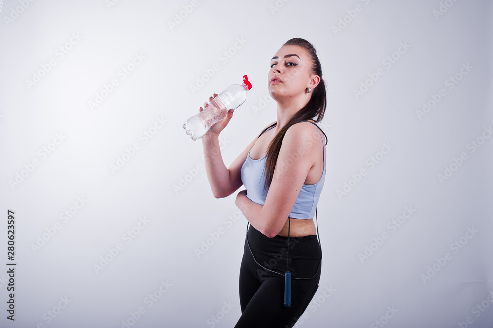 Cheerful attractive young fitness woman in top and black leggings with jump rope and bottle of water isolated over white background. Cheerful attractive young fitness woman in top and black leggings with jump rope and bottle of water isolated over white background.