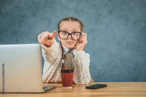 Cute little schoolgirl points finger straight, isolated on grey background. Schoolgirl with laptop pointing her finger.