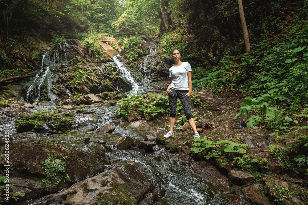 Beautiful girl at a small waterfall, Carpathian mountain stream. Travel concept, leisure activity, vacation