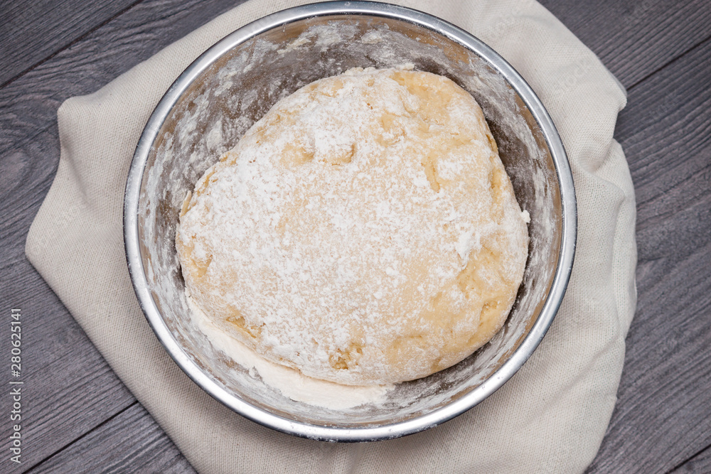 The ball of raw dough for pizza or bread in metal plate on wooden background. Flat lay, top view.