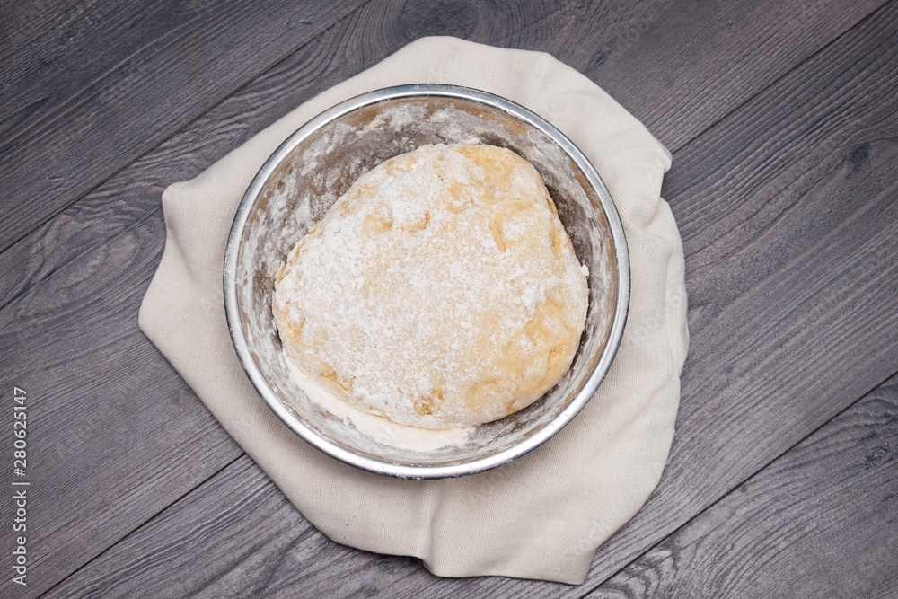 The ball of raw dough for pizza or bread in metal plate on wooden background. Flat lay, top view. The ball of raw dough for pizza or bread in metal plate on wooden background. Flat lay, top view.
