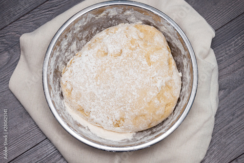 The ball of raw dough for pizza or bread in metal plate on wooden background. Flat lay, top view.