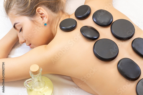 Spa hot stone massage. Professional beautician massaging female back by stones. Relaxed girl enjoying body treatment at wellness center