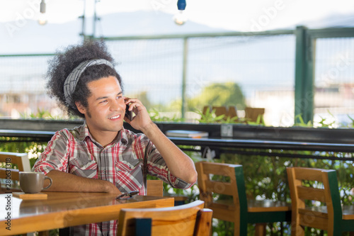 Young man enjoys his coffee at a cafe during a break from work while he is speaking on his phonee photo