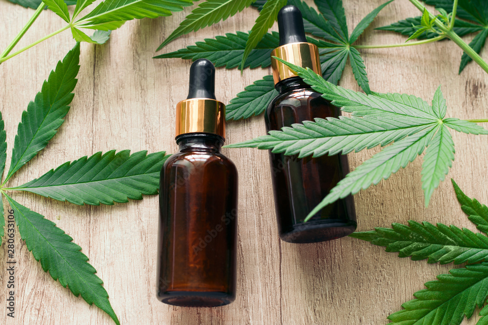 natural herbal hemp essential oil in a glass bottle and marijuana green leaves on a wooden background top view flat lay - obrazy, fototapety, plakaty 