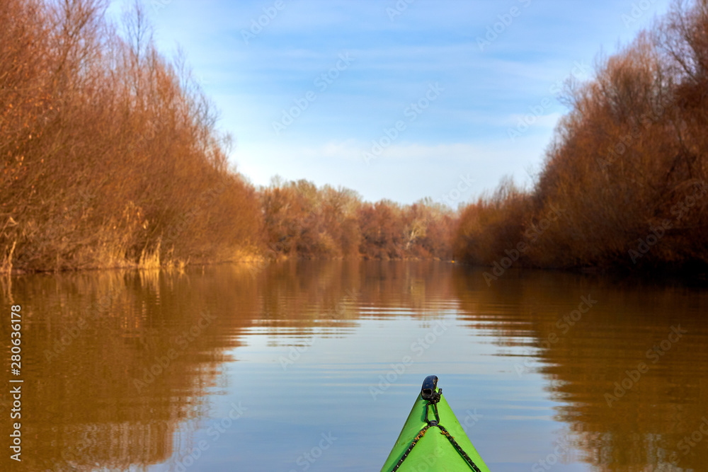 Kayaking on green kayak along the autumn river with brown trees on the shoreline at clear autumn day. Autumn kayaking. Autumn or winter kayaking. Kayaking on green kayak along the autumn river with brown trees on the shoreline at clear autumn day. Autumn kayaking. Autumn or winter kayaking.