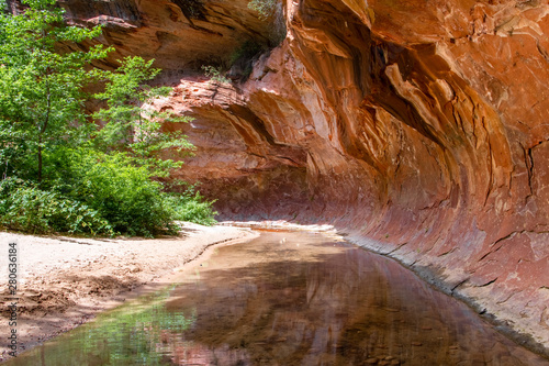 Tranquil stream flows through a tunnel of overhanging red rock standstone in a canyon in the American Southwest - Oak Creek, Sedona, Arizona
