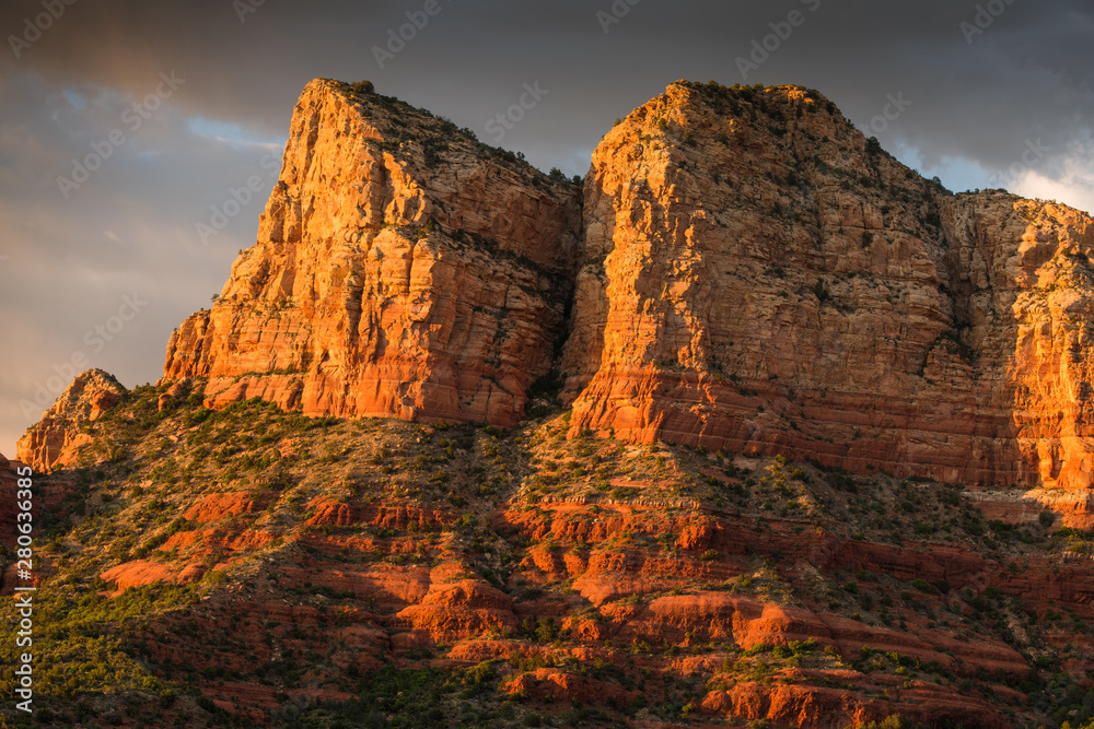 The light of sunset illuminates a high rock formation under a dramatic sky - Sedona, Arizona