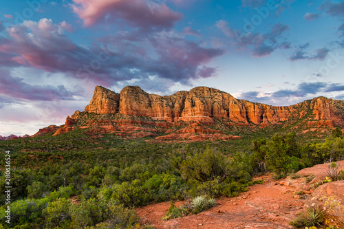 Sunset illuminates a beautiful vast landscape of red rock formations and green juniper tree forest below a blue sky with colorful pink and purple clouds - Sedona, Arizona
