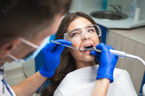 dentist in mask filling the patient's root canal while she is lying on dental ch Fototapeta