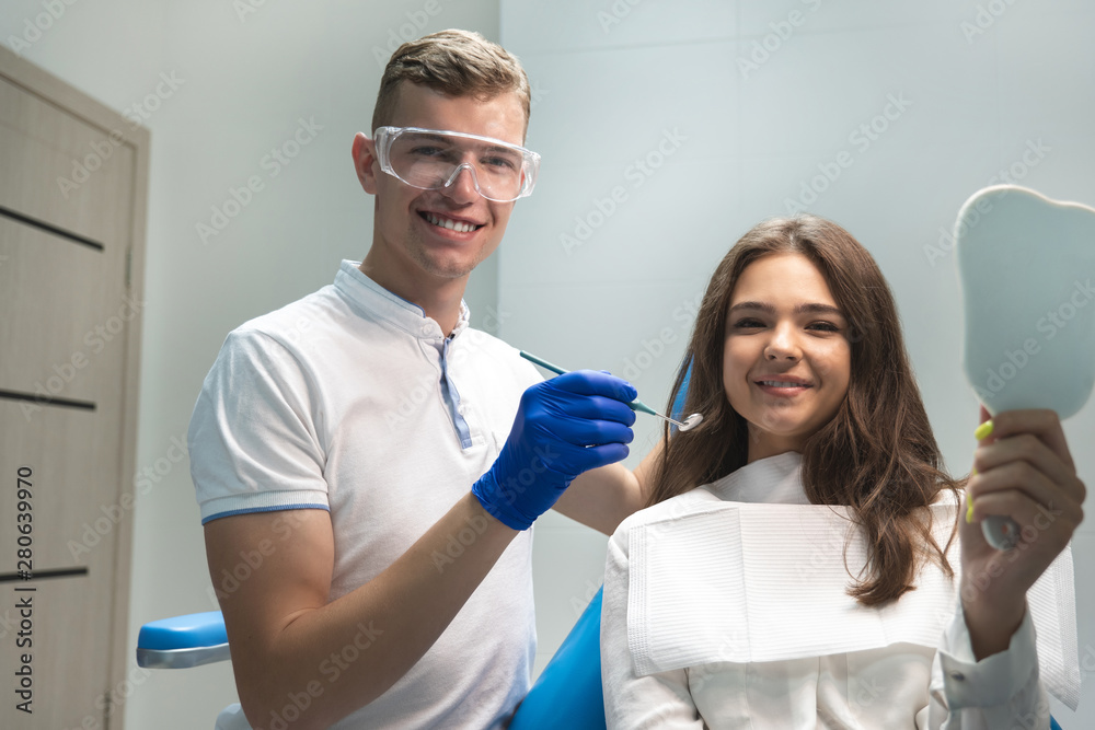 Obraz premium young brunette woman patient and dentist in blue gloves medical mask and safety glasses looking happy with treatment results in dental clinic