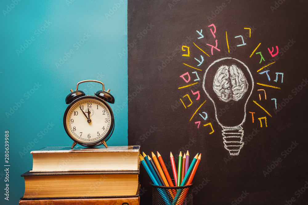 Book, alarm clock, pencils and light bulb with human brain and Hebrew letters on chalkboard