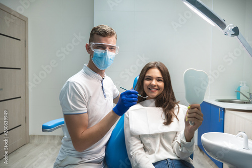 young brunette woman patient and dentist in blue gloves medical mask and safety glasses satisfied checking treatment results in dental clinic