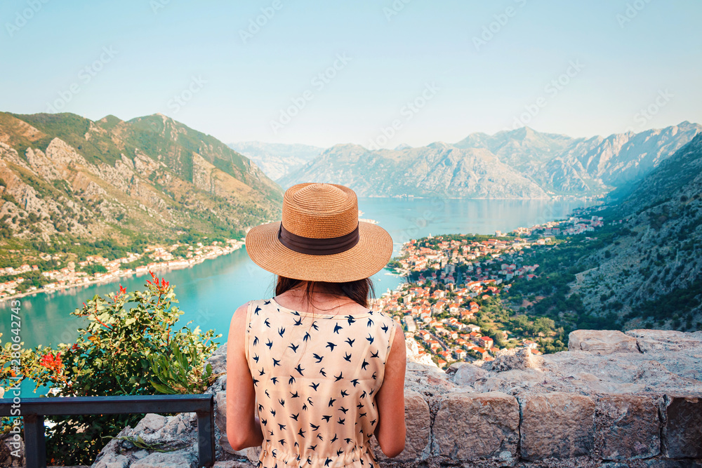 Rear view of young woman in dress and hat, who looking from above to the Kotor city and Boka bay, Montenegro