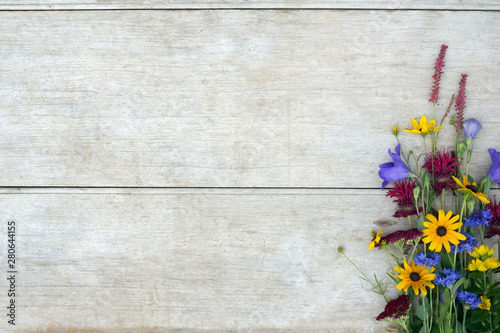 Horizontal image of a colorful bunch of bright summer flowers against a weathered wood background, with copy space