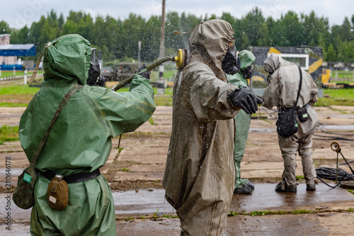 A soldier in a chemical protection suit cleans another soldier