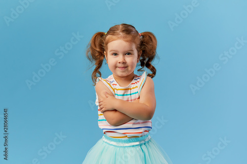 Portrait of surprised smiling cute little toddler girl child standing isolated over blue background. Looking at camera. 