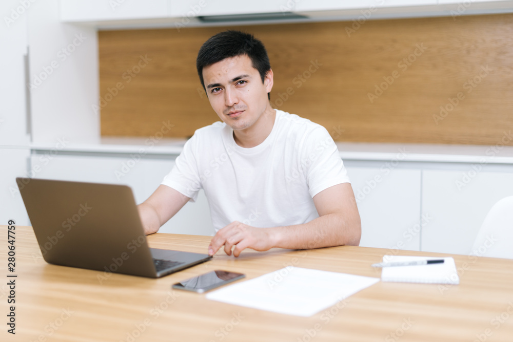 Serious young businessman is working with laptop in cafe and looking at camera Serious young businessman is working with laptop in cafe and looking at camera