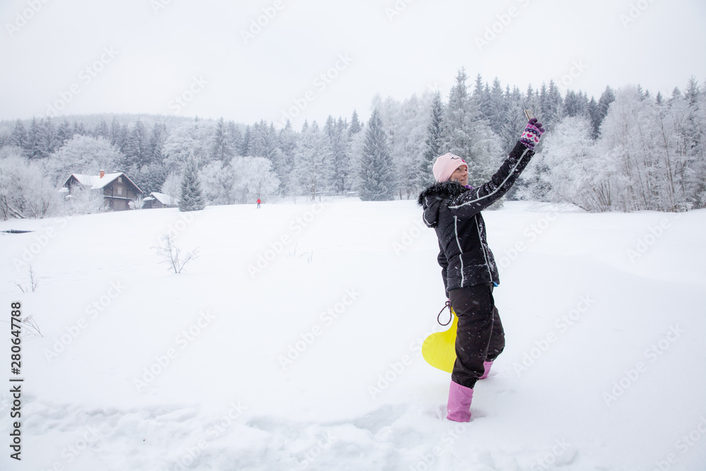 woman playing with her dog on snow in winter. taking pictures by phone selfie