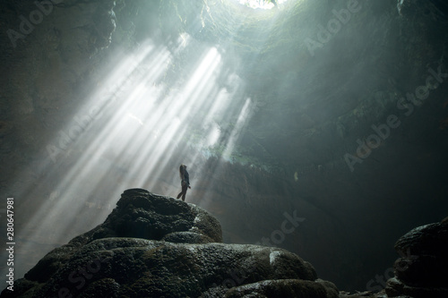 Girl stands under the rays of light in a deep cave Jomblang Cave. Java, Indonesia photo