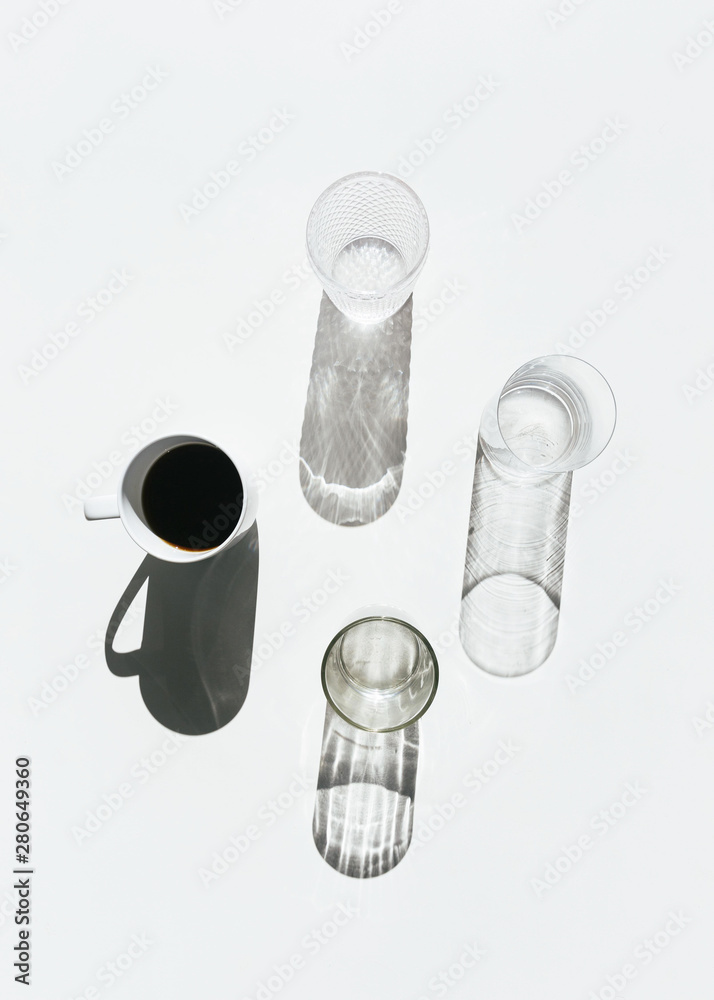 Still life with coffee cup, spoon, glasses, light and shadow on white background