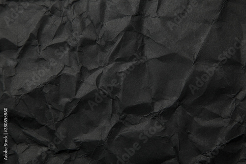 Texture of black crumpled paper. Dark paper background with chaotic bends. A sheet of black wrinkled paper