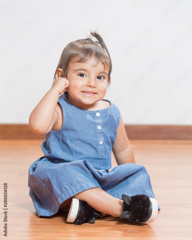 Baby girls of two poses for studio portraits. She is wearing a jean dress. She is sitting on the floor. Baby girls of two poses for studio portraits. She is wearing a jean dress. She is sitting on the floor.